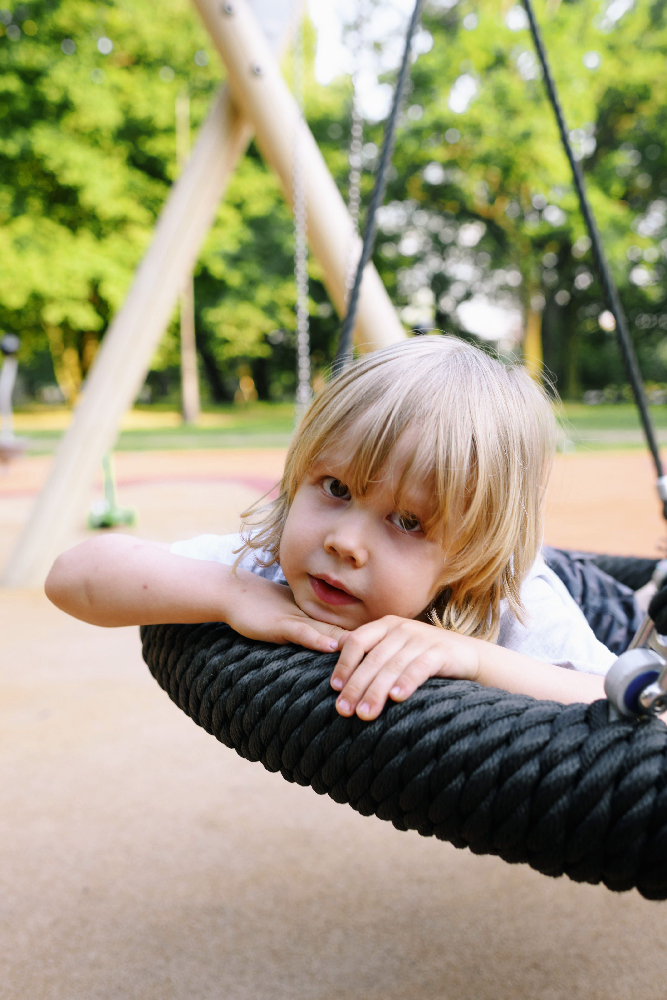 Child relaxing on a commercial nest swing featuring a large shared platform designed for inclusive playground play.